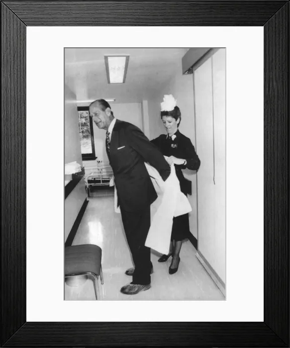 Framed Print : The Duke of Edinburgh. Prince Philip being helped with his protective clothing by Matron