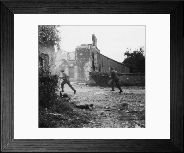 Framed Print : A Bren gunner covers the roadway while men move along the street of the village of Hottot