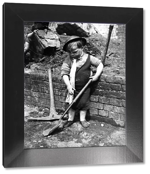 A little boy pays with a shovel following air raid attacks in England. Circa 1941