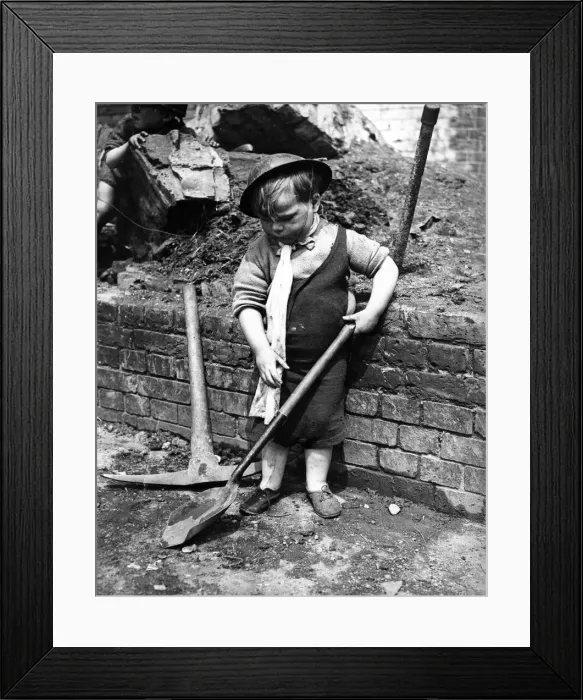 Framed Print : A little boy pays with a shovel following air raid attacks in England. Circa 1941 Framed Print : A little boy pays with a shovel following air raid attacks in England. Circa 1941
