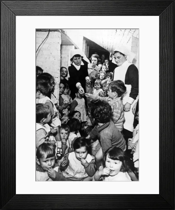 Framed Print : A nursing sister distributes sweets to these young children while they sit in a wine