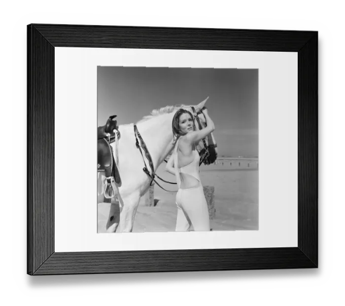 Framed Print : Diana Rigg, who plays Emma Peel, looking serious to camera with a white horse