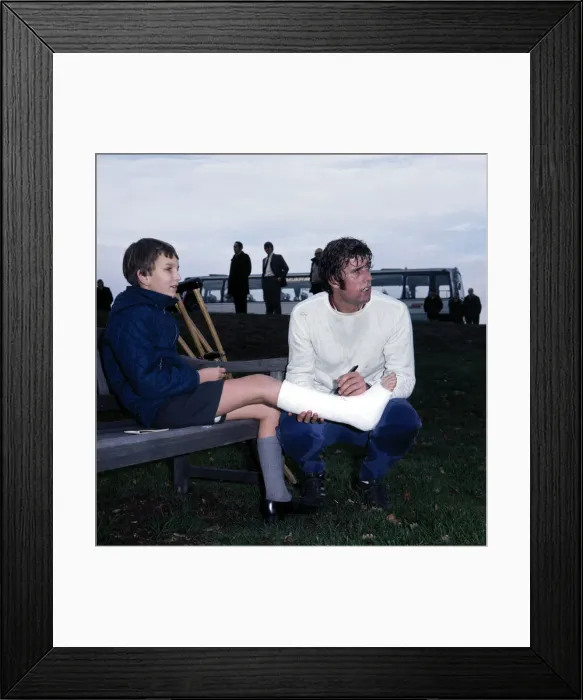 Framed Print : England footballer Geoff Hurst signs an autograph for a young fan in plaster caste during Framed Print : England footballer Geoff Hurst signs an autograph for a young fan in plaster caste during