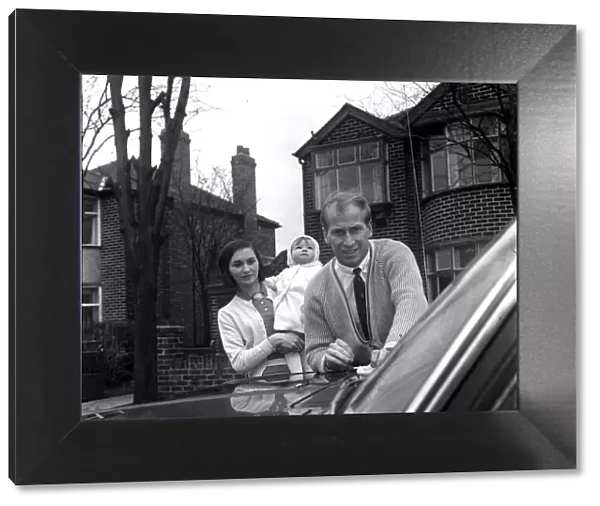 Bobby Charlton washes his car, watched by wife Norma Charlton who is holding their baby