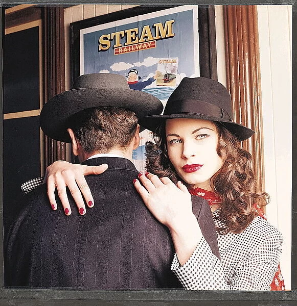 1940s dress fashion - Female model wearing black hat with her arms around male model