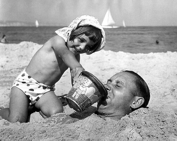 4 year old Gloria Smart gives her dad a drink of seawater after burying him in the sand