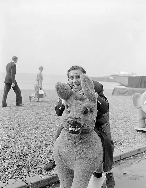 Actor and comedian Norman Wisdom photographed on Brighton Beach on a stuffed donkey