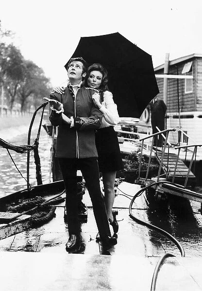 Actor Roger Moore and Claudia shelter under an umbrella from the rain showers at Chelsea