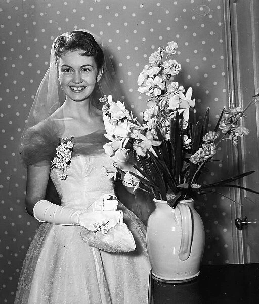 Actress Janette Scott holding a vase of flowers wearing a wedding dress