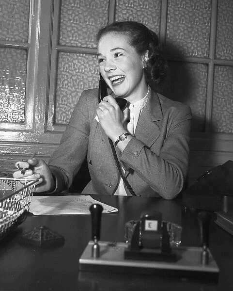 Actress Julie Andrews talking on the phone behind her desk January 1954
