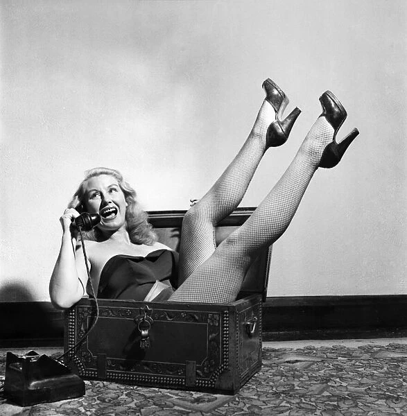 Actress June Cochrane sitting in a chest talking on the telephone. October 1952 C5181