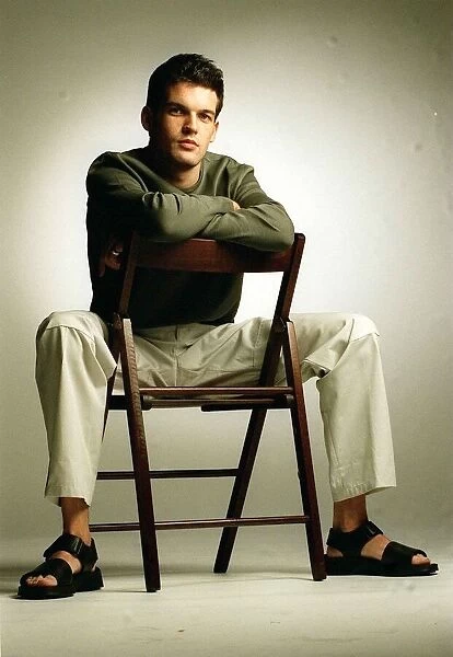 Adam Sinclair actor sitting on chair January 1999 wearing green jumper cream trousers