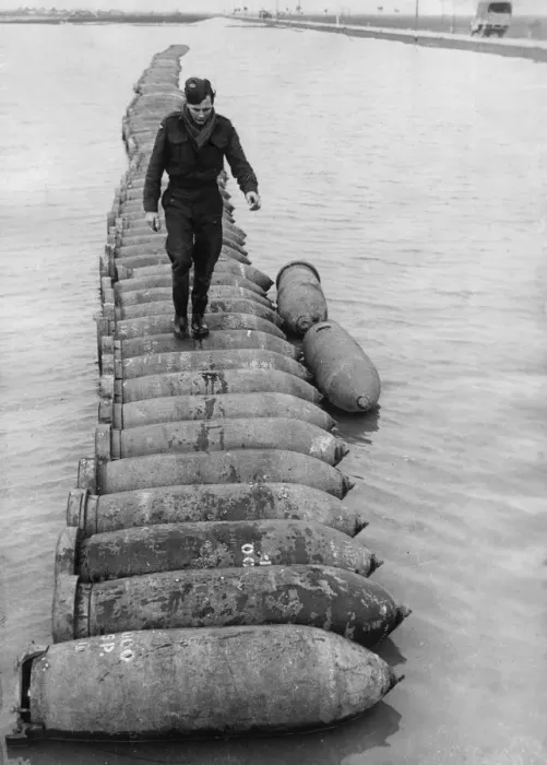 Framed Print : An airman using a line of 1000 lb bombs as a bridge to cross a flooded airfield at an RAF Framed Print : An airman using a line of 1000 lb bombs as a bridge to cross a flooded airfield at an RAF