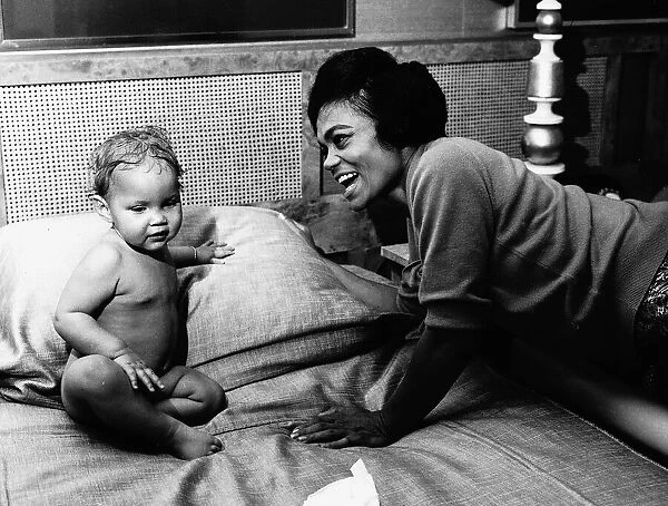 American singer and actress Eartha Kitt, photographed with her baby girl Kitt on her bed