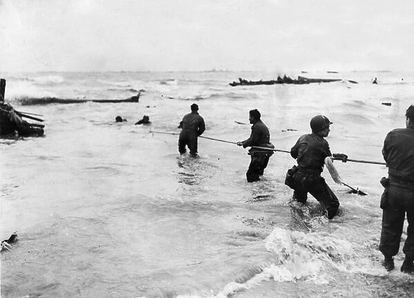 American soldiers waist deep in water, man a lifeline rigged from a swamped landing craft
