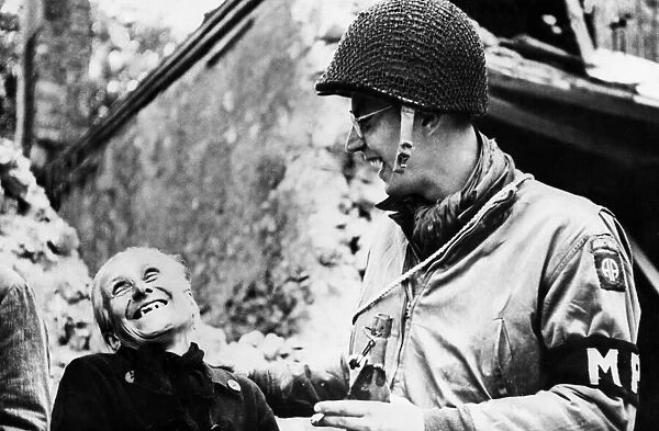 An American troop shares a joke with a civilian while on duty. 22nd June 1944