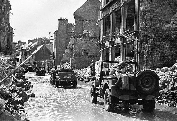 American troops in jeeps making their way through a bomb damaged Normandy town in