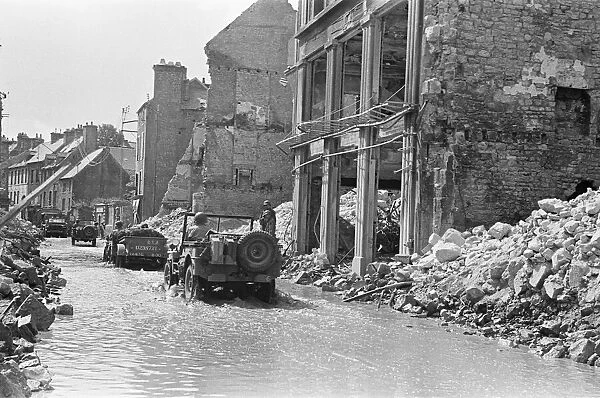 American troops pass through the ruined buildings and wrecked German transport in