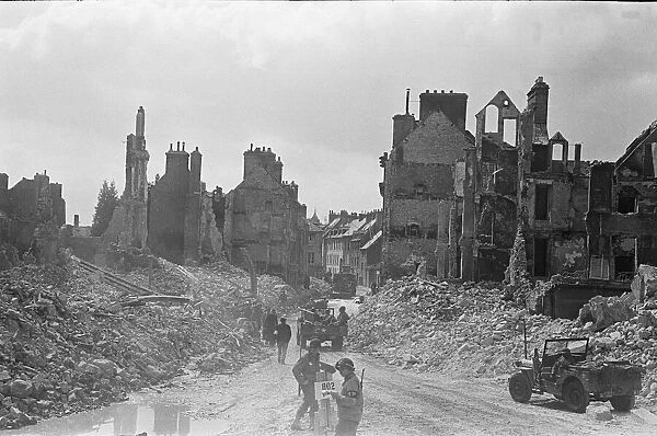 American troops pass through the ruined buildings and wrecked German transport in