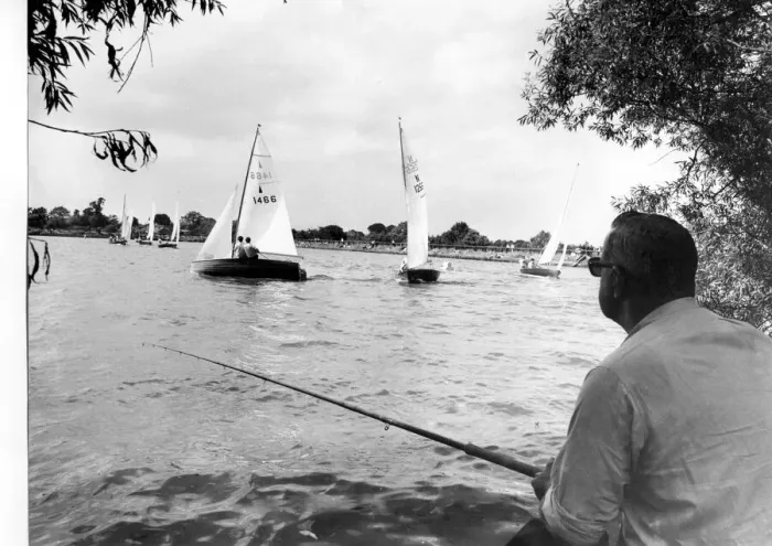 Framed Print : Angling. Under the cool shade of trees, a fisherman looks on at yachts as they cut Framed Print : Angling. Under the cool shade of trees, a fisherman looks on at yachts as they cut