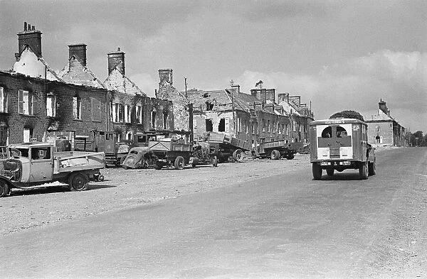 A US army ambulance drives pass the ruined buildings and wrecked German transport in