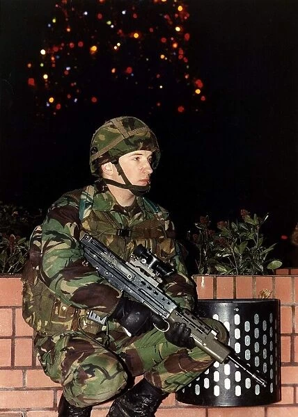 Army Soldier in camouflage uniform standing with a firearm in front of a Christmas tree