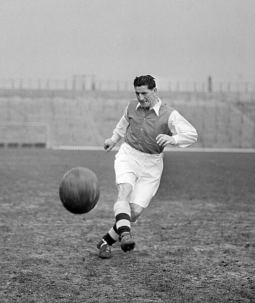 Arsenal Football player Ronnie Rooke kicking football with the north bank terracing