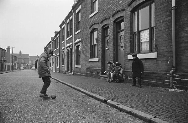 Two asian boys playing football in the street while their friends look on in Marshall