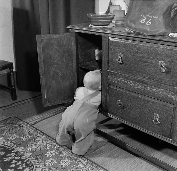 Baby boy looking in the cupboards at his home. October 1952 C5534
