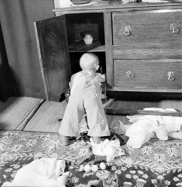 Baby boy looking in the cupboards at his home. October 1952 C5534-004