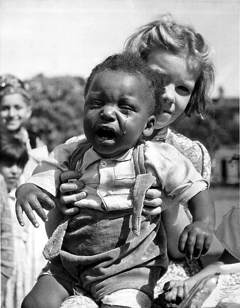 A Baby crying being held by a young girl at a festival tea party July 1953
