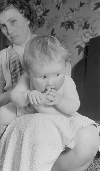 Baby sitting on mothers lap chewing her toes. 23rd May 1952 Local Caption