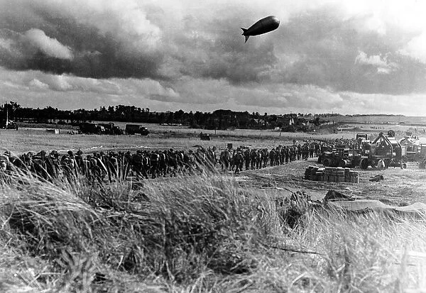A barrage balloon floats overhead as British troops march towards the front line in