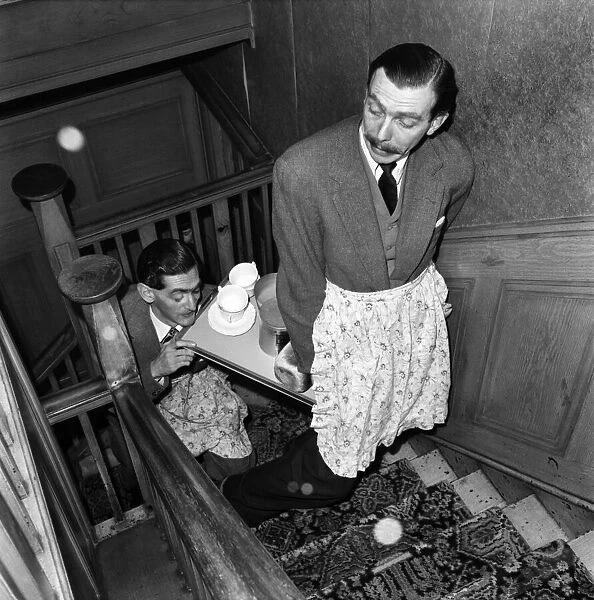 BBC comedy scriptwriters Frank Muir and Denis Norden bringing a tray of tea up the stairs