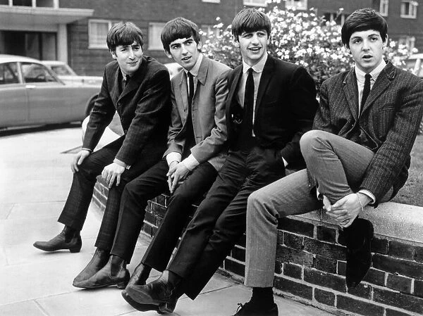 The Beatles pose sitting on a wall. Left to right: John Lennon, George Harrison