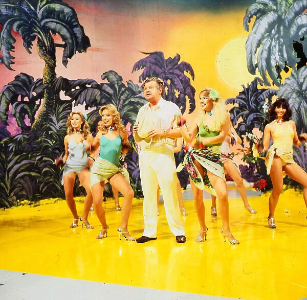 Benny Hill comedian 1989 With girls dancing on stage desert island palms trees set