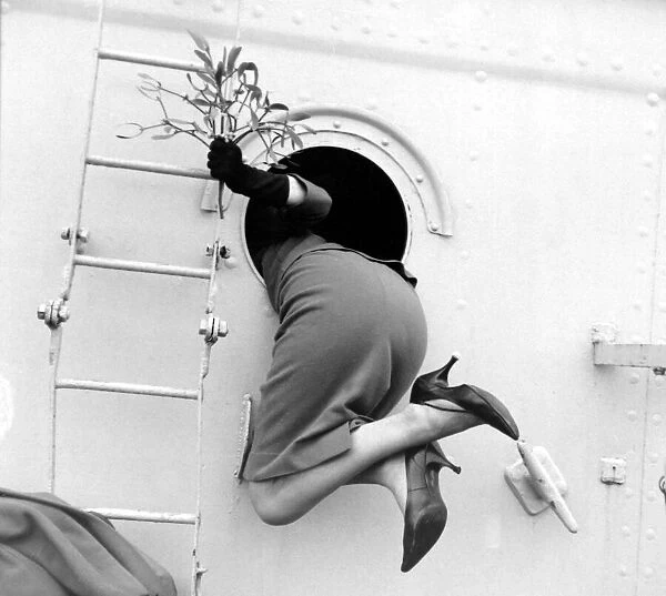 Beverley Janner holding mistletoe is pulled through a porthole by her sailor husband to