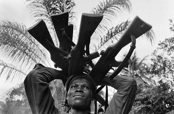 A Biafran soldier seen here holding a selection of guns during the Biafran conflict