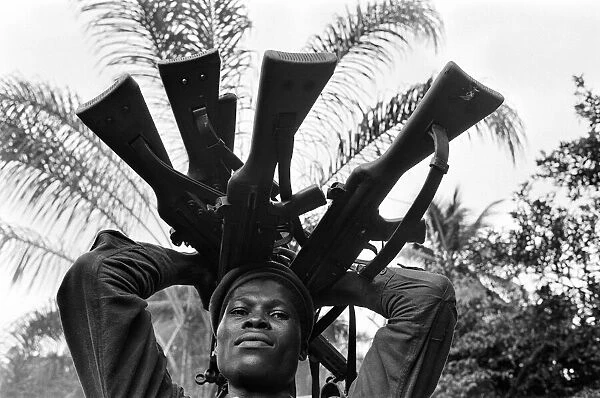 A Biafran soldier seen here holding a selection of guns during the Biafran conflict