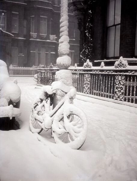 A bicycle leans against a lamp-post covered in thick snow January 1954