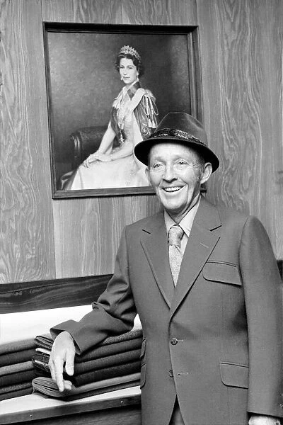 Bing Crosby pictured in the exclusive tailors shop infront of a portrait of HM The