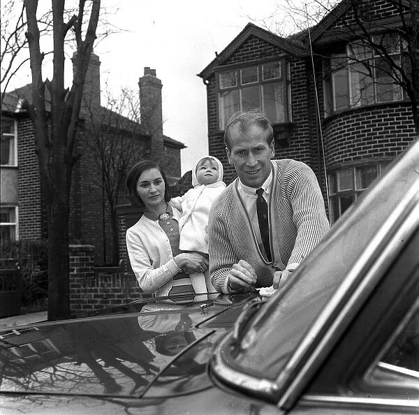 Bobby Charlton washes his car, watched by wife Norma Charlton who is holding their baby