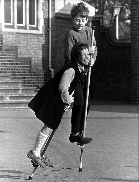Boy and girl on pogo sticks in the playground. 22nd March 1967