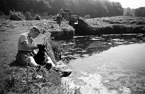 A boy sits with his pet dog next to the River Chess in Chenies, Buckinghamshire