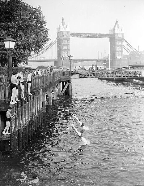 Boys jumping off the bank of the River Thames into the water on hot summers day near