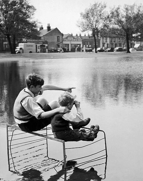 Two boys sitting on an old fire guard on the edge of a lake. 1st July 1955