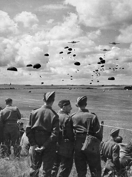 British army soldiers watch paratroops descending from aircraft during a demonstration in