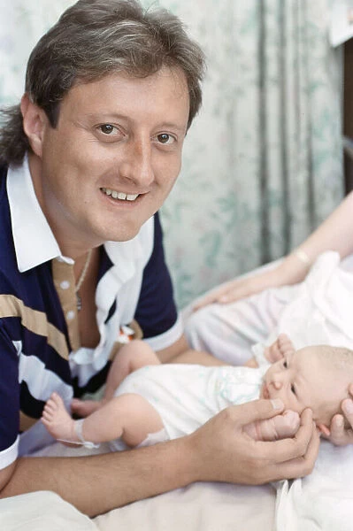 British darts player Eric Bristow poses at home with his new born baby girl who has been
