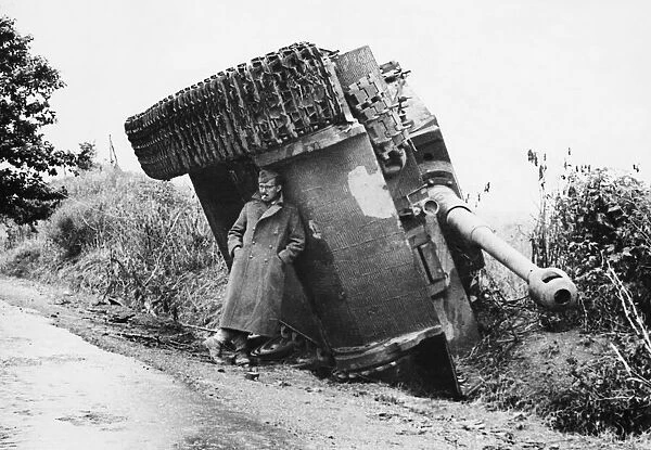 British soldier shelters from the rain under the tracks of a disabled Mark 6 German Tiger