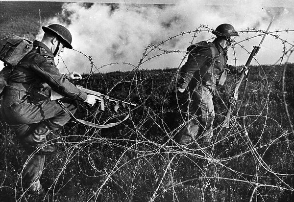 British troops advancing through barbed wire during a training drill. September 1943
